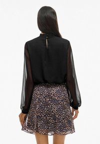 Blusa nera in chiffon con collo alto arricciato, abbinata a una mini gonna svasata con stampa animale in marrone scuro e crema.