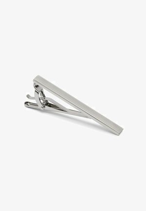 Silverfärgad slipsklämma med en slank, avlång form som har vertikala ribbor. Den polerade metallytan reflekterar ljus och förbättrar dess rena design.