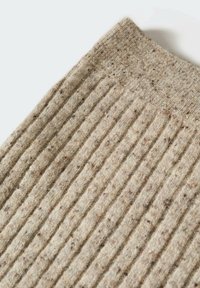 Tissu tricot côtelé beige avec une texture tachetée, montrant un bord plié sur un fond blanc.