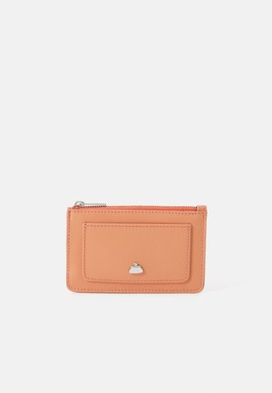 Cartera de cuero color durazno con cremallera en la parte superior, que cuenta con un bolsillo frontal y un detalle plateado en forma de bolso. Textura suave.