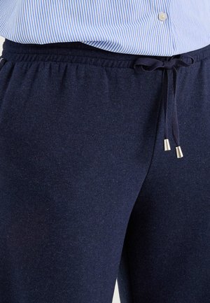 Camisa de rayas azules metida dentro de pantalones deportivos azul marino con cordón atado en un lazo en la cintura.