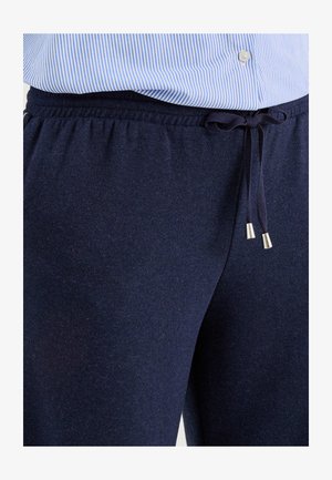 Camisa de rayas azules metida dentro de pantalones deportivos azul marino con cordón atado en un lazo en la cintura.