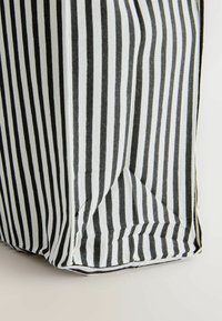 Borsa tote riutilizzabile con strisce verticali bianche e nere. Realizzata in tessuto, presenta una base quadrata e una trama leggermente stropicciata.