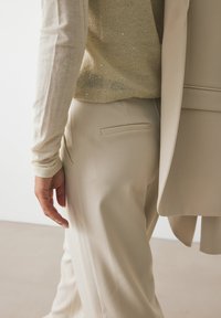 Pantalons beiges ajustés avec poches latérales, associés à un haut en tricot texturé beige clair doté de petites sequins. Tissu lisse, coupe décontractée.