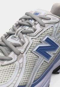 Κοντινό πλάνο ενός αθλητικού παπουτσιού σε λευκό και ανοιχτό μπλε χρώμα με γκρι κορδόνια και υφή από πλέγμα, που φέρει ένα μπλε λογότυπο στο πλάι.