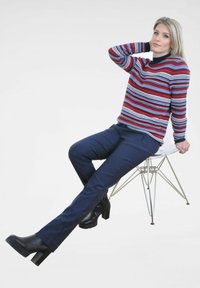 Gestreepte gebreide trui in rood, blauw en wit; marineblauwe broek; zwarte block-heeled laarzen; zittend op een heldere acrylstoel; neutrale achtergrond.