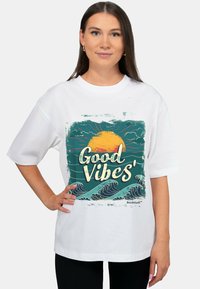 Witte T-shirt met korte mouwen met een kleurrijk grafisch ontwerp van golven en een zon, met de tekst "Good Vibes". Soepele katoenstructuur.