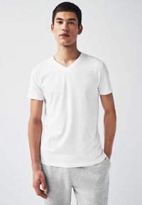 T-shirt bianca a scollo a V in cotone, maniche corte, texture liscia. Abbinata a pantaloni della tuta grigio chiaro, entrambi progettati per un uso casual.