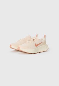 Helles rosa Sportschuhe mit einem strukturierten Obermaterial, ausgestattet mit einer beigen Außensohle und einem kontrastierenden korallenfarbenen Swoosh-Logo an der Seite.