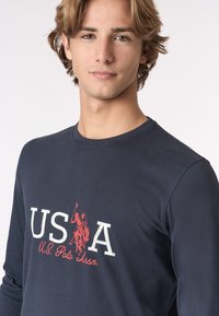 Maglietta a maniche lunghe blu navy con un logo bianco e rosso che recita "USA" e un'immagine di un giocatore di polo, con scollatura rotonda e texture morbida.