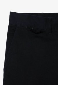 Pantaloni in denim blu scuro con cintura, tasche frontali e dettagli di cucitura discreti. Il materiale ha una texture liscia e una forma strutturata.