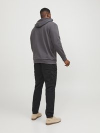 Grijze hoodie met een capuchon, gecombineerd met zwarte cargobroeken met meerdere zakken. Tan gekleurde schoenen met een gestructureerde uitstraling maken de outfit compleet.