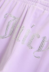 Svetlo vijolično blago s srebrnimi kristalčki, razporejenimi v besedo "Juicy" v dekorativni pisavi s kurzivo.