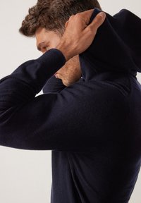 Marinblå huvtröja i mjukt material, med en figursydd design och texturerade ärmdekorationer. Huvan är draget över huvudet.