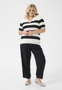 Top cu decolteu în V, dungat în crem și negru, cu mâneci scurte, combinat cu pantaloni negri largi și pantofi flata deschiși la culoare.