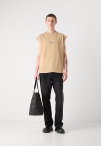 Beige tílko bez rukávů, černé džíny, černá kožená taška a boty se zelenými akcenty. Jednoduchý design, ležérní střih, hladká textura látky.