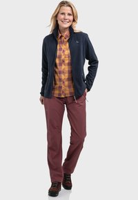 Fleecejacke in Marineblau, karierter Hemd in Orange und Gelb sowie bordeauxrote Hose. Ausgestattet mit stabilen Stiefeln mit Schnürsenkeln und einem Logo auf der Jacke.