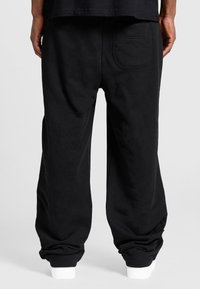 Black sweatpants made from cotton blend; feature a relaxed fit, elastic cuffs, and a single patch pocket on the back.