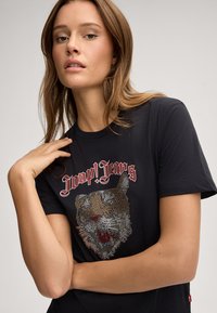 T-shirt noir avec un graphique de tigre en strass et le texte rouge "Joop! Jeans" au-dessus. Manches courtes et col rond.