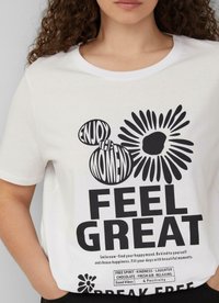 Witte katoenen T-shirt met opvallende zwarte tekst en grafische elementen, waaronder een bloemenontwerp en motiverende zinnen in diverse lettertypen.