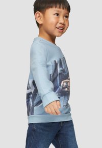 Lichtblauwe sweatshirt met een stadsafbeelding, ronde halslijn en ribgebreide manchetten. Gecombineerd met donkere spijkerbroek.