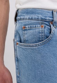 Jeans in denim azzurro chiaro con taglio dritto, caratterizzati da rivetti in ottone, tasche anteriori e posteriori e una texture sbiadita.