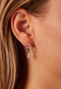 Zilveren oorring met een kleine peervormige heldere edelsteen, versierd met tiny rhinestones langs de rand van de oorring.