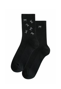 Schwarze Knöchelsocken mit gerippter Textur, die auf dem oberen Abschnitt verstreute silberne Rippendesigns aufweisen.