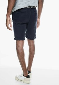 Marineblauwe katoen shorts met opgerolde cuffs, achterzakken en een patroonriem. Gedragen met witte sneakers met zwarte accenten.