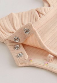 Krupni plan bež rebrastog tkanja s tri metalna kopče na pritisak i mekanim podstavom ukrašenim malim ružičastim otiscima jagoda.