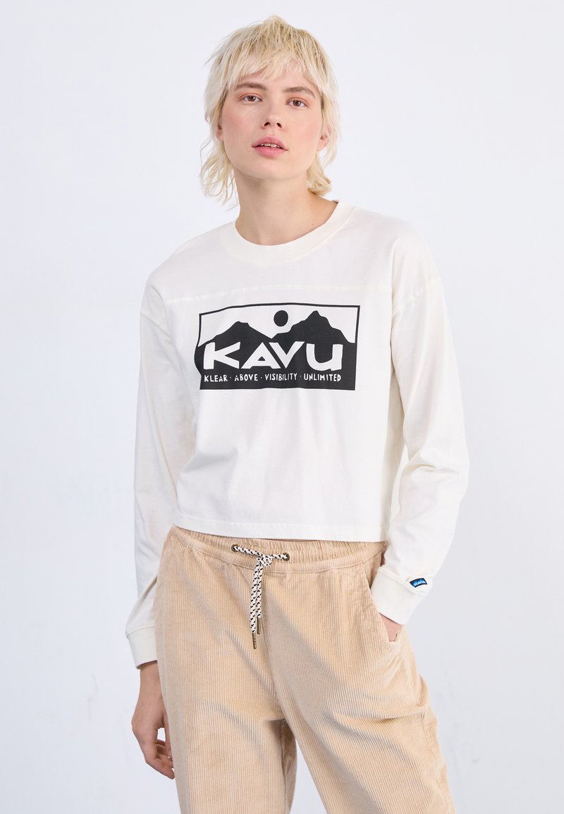 Weißes Langarmhemd mit schwarzem Berggrafik und "KAVU"-Text. Kombiniert mit beigen Cordhose mit Kordelzug.
