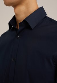 Mornarsko modra srajca z dolgimi rokavi, s strukturiranim ovratnikom in gumbi; ima gladko, lahkotno tkanino in diskretne šive.