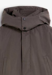 Chaqueta acolchada marrón con alto cuello y dos botones a presión negros, que incluye bolsillos laterales y un acabado liso y mate.