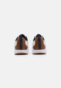 White sneakers with brown and navy accents, featuring a textured upper, low-profile design, and rubber sole with a patterned tread.