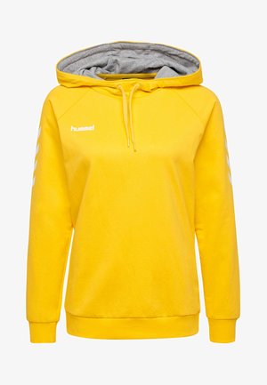 Żółta bluza z kapturem z szarym wykończeniem wewnątrz. Posiada białe logo oraz wzór chevron na rękawach. Wykonana z miękkiego materiału, luźny krój.