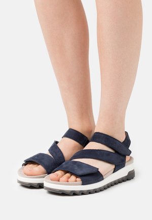 Mørkeblå ruskindsandaler med brede krydsremme, åben tå-design og en struktureret hvid gummisål. Har justerbar rem for pasform.