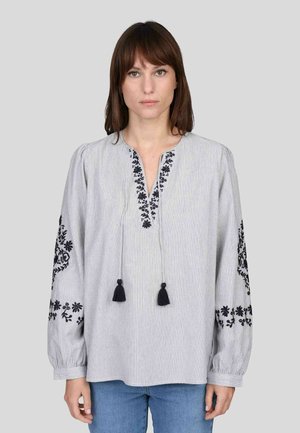 Chemisier rayé blanc et marine, avec broderies florales noires sur les longues manches et des franges au col. Matériau en coton doux.