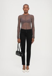 Átlátszó barna, hosszú ujjú blúz gombos részletekkel, fekete skinny farmerral párosítva. A modellen egy kis fekete táska és fehér magassarkú cipő található.