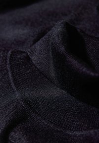 Schwarzer Stoff mit einem weichen, strukturierten Strick, der Falten und unterschiedliche Farbtöne zeigt, die die Tiefe betonen. Das Material wirkt glatt und flexibel.