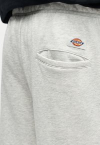 Pantalon de survêtement gris clair avec poche arrière et ceinture élastique, arborant une petite étiquette rectangulaire avec le logo Dickies au-dessus de la poche.