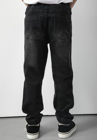 Czarne dżinsy o luźnym kroju, z elastycznym pasem, dwiema tylnymi kieszeniami i mankietami. W połączeniu z czarnymi trampkami.