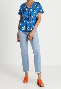 Blue floral blouse with a v-neck and short sleeves, paired with light blue jeans. Orange open-toe slides complete the outfit.