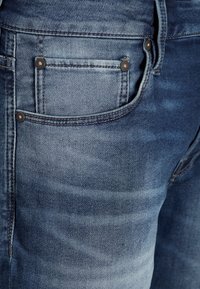 Džínové kalhoty světle modré barvy s vybledlým povrchem, s zadní kapsou se švy a kovovými nýty. Texturovaná tkanina.