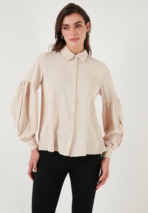Beige button-up blouse with a collar and puffed long sleeves. Smooth fabric with a relaxed fit, featuring a straight hemline.
