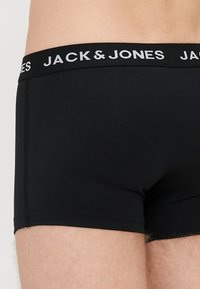 Črne bombažne boksarice z elastičnim pasom. Elastični pas nosi napis "JACK & JONES" v sivi barvi. Gladka tekstura in prilegajoč dizajn.