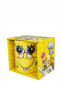 Mug in ceramica gialla con il volto di un personaggio dei cartoni animati, dotato di grandi occhi blu, lentiggini e una bocca sorridente. Confezionato con grafiche colorate.