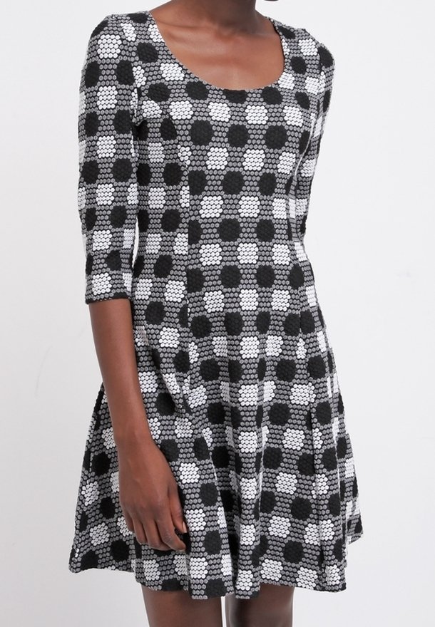 Czarna i biała sukienka w kropki z dopasowaną górą i rozkloszowanym dołem, z rękawami o długości trzech czwartych i dekoltem w serek.