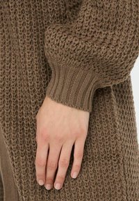 Cardigan marrone lavorato a maglia con un motivo a punto testurizzato e polsini a costine, che presenta un design caldo e voluminoso con un'aspetto morbido.