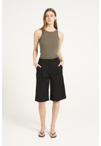 Pantaloni corti neri sartoriali con pieghe frontali, tasche e una vestibilità rilassata. Abbinati a una maglietta senza maniche in cotone ribbed verde oliva.