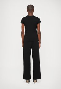 Camiseta negra ajustada de manga corta combinada con pantalones negros de pierna ancha, llevada con zapatos de tacón alto negros; textura de tela suave.